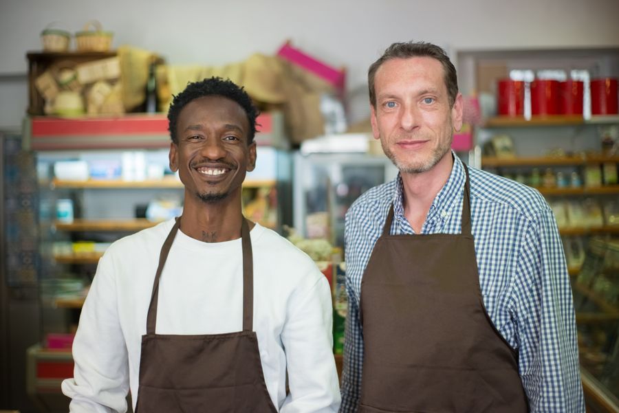 Two smiling shop owners in aprons inside their local store